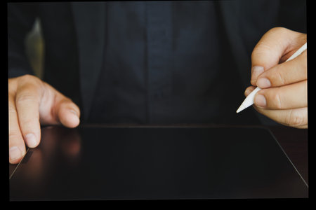 Close up a man in a black shirt holding an electronic pen to write on a tablet on a wooden table