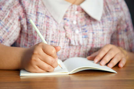 An Asian woman in casual clothes looking at a camera while using an electronic pen on a tablet on a wooden tableの写真素材