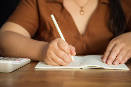 Close-up of an Asian woman taking notes on a notebook on a wooden table.