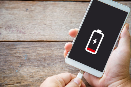 Close up a man hands plugging a charger on a smart phone on a wooden tableの写真素材