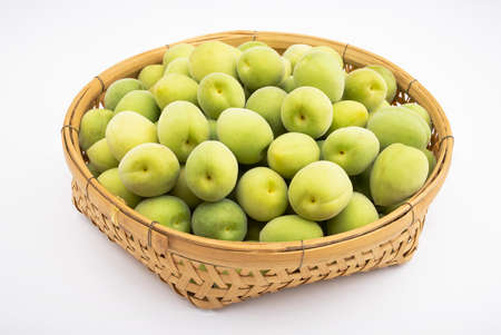 Green plum fruits or Japanese apricot in bamboo basket on white backgroundの写真素材