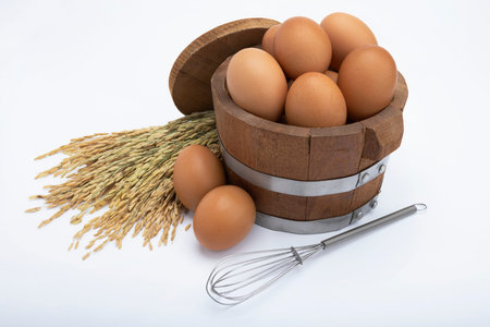 Chicken eggs in wooden bucket and ear of rices on white background