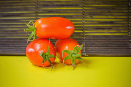 Wet red tomatoes lie on yellow surfaceの写真素材