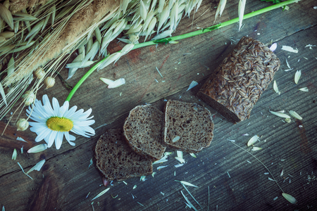 Natural background- rustic mood. Still life: sheaf of oats, sliced brown bread, daisyの写真素材