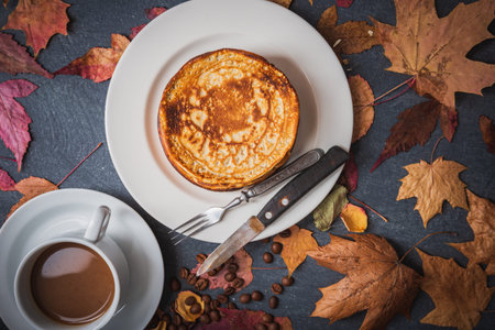 Still life on an autumn theme breakfast. Delicious pancakes on white dishes and yellow leaves