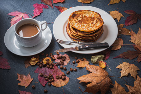 Still life on an autumn theme breakfast. Delicious pancakes on white dishes with cup of coffee and yellow leaves.の写真素材