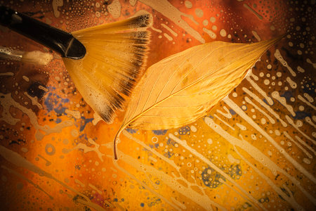 Old paint brush and autumn leaf on abstract yellow and orange background.の写真素材