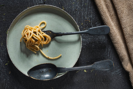 Still life - pasta in a plate and a fork with a spoon on the table. Food on a dark backgroundの写真素材