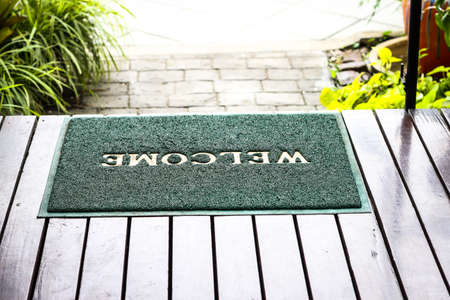 Green doormat with welcome text on wooden floor in the gardenの写真素材