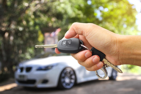 Man holding car key on blurred background, closeup. Car rental