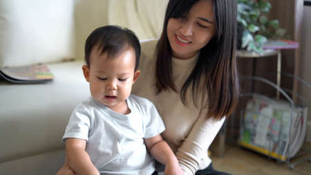 Young mother and little boy child reading book sitting on floor near sofa.の写真素材