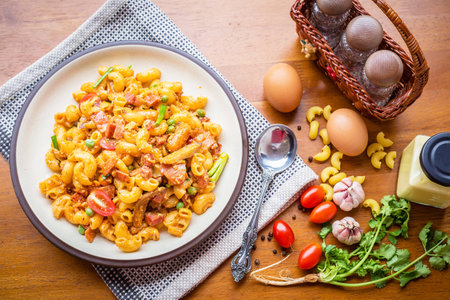 fried macaroni with egg pork ham and vegetable in tomato sauce in plate placed on a wooden table.の写真素材