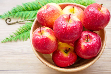 Fresh red Apples in wooden bowl on brown wooden backgroundの写真素材
