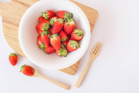 Fresh strawberries in white bowl on wooden platter with wooden spoons on white background.の写真素材