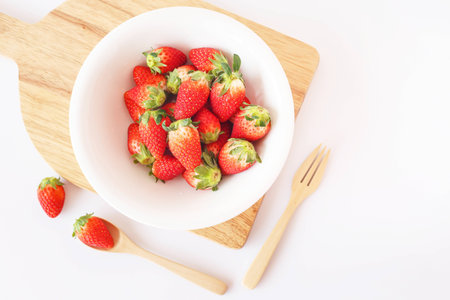 Fresh strawberries in white bowl on wooden platter with wooden spoons on white background.の写真素材