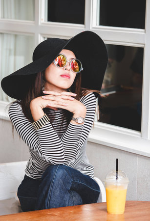Beautiful Asian girl sitting in modern cafe with orange juice and feeling relaxの写真素材