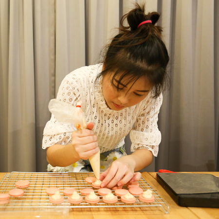 Squeeze the worms into the middle of macaron. woman enjoy to preparing macarons at home, top view, retro tonedの写真素材