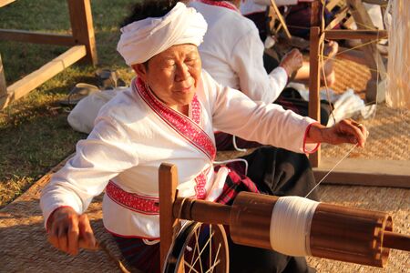 Old woman dressed in white indigenous dress, sitting thread in the traditional way of the natives, 14 Apr 2017, Lamphun Thailandのeditorial素材