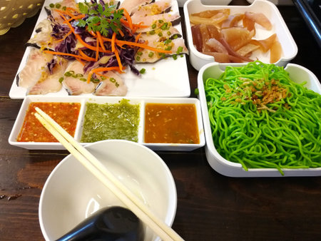 sashimi, vegetables, noodle and bowls with spoon and chopsticks are placed on the table.