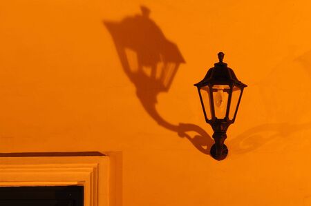 An old street lamp shadowed on orange wallの写真素材