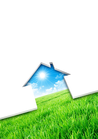 Eco house concept. Cutting of a blank sheet, house shaped above a green field backgroundの写真素材