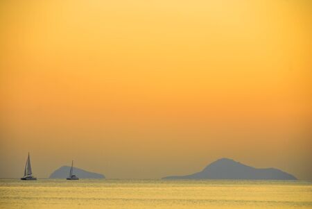Sailboat off in the distance under the setting sun near Santorini, Greeceの写真素材