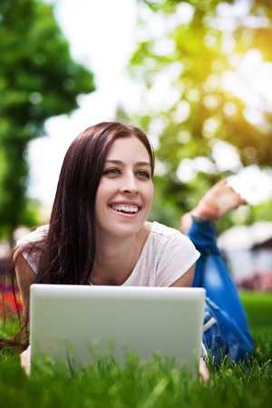 smiling girl laying on grass with laptopの写真素材