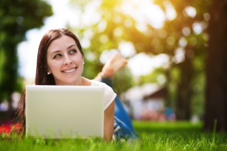 Happy smiling girl laying on the green grass with laptopの写真素材