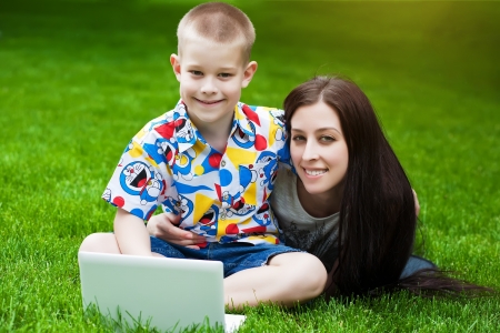 smiling Mother and son  in the green grass with laptopの写真素材