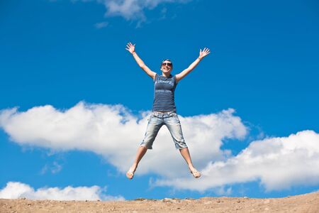 jumping girl with hands up against  blue skyの写真素材