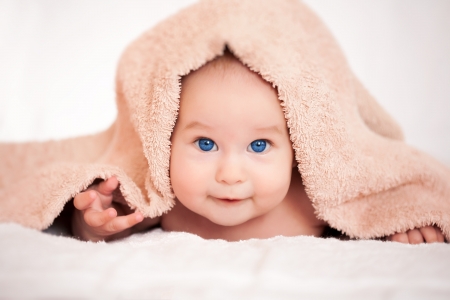 baby is hiding under the beige terry towelの写真素材