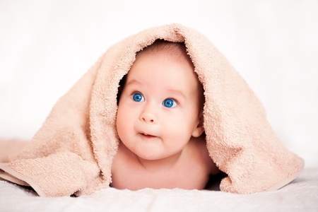 cute baby girl is hiding under the beige terry towelの写真素材