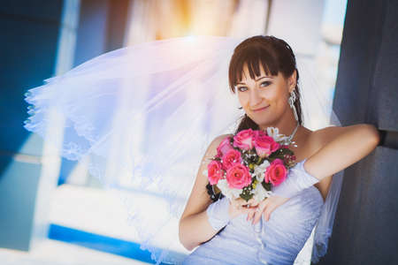 happy bride in white dress against a blue modern building backgroundの写真素材