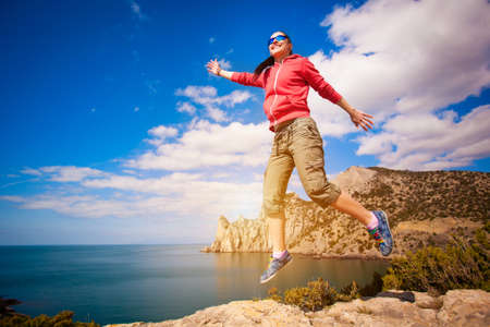 Young girl jumping on a rock against the blue skyの写真素材