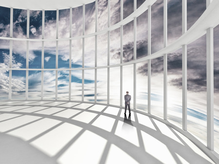 businessman standing in office and looking at sky in windowの写真素材