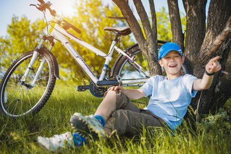 happy kid with a bicycle resting under a treeの写真素材