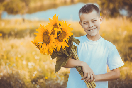 Happy kid with bouquet of beautiful sunflowers against summer fieldの写真素材