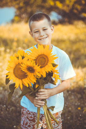Happy kid with bouquet of beautiful sunflowers against summer fieldの写真素材