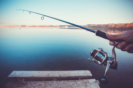 hand with spinning and reel on the summer lakeの写真素材