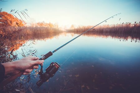 hand with spinning and reel on the summer lakeの写真素材