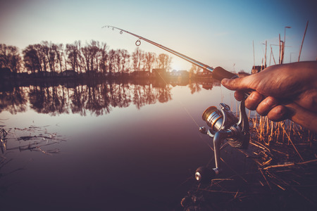hand with spinning and reel on the summer lakeの写真素材