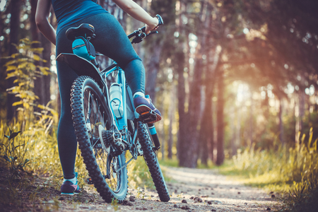 low angle view of cyclist riding mountain bike in the forest at sunsetの写真素材