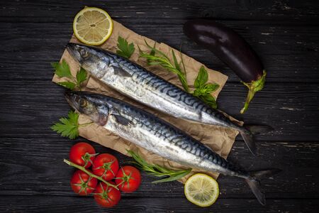 Mackerels served on the black table with lemon, tomatoes, eggplant, and herbsの写真素材