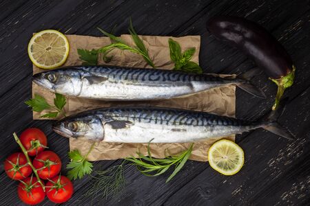 Mackerels served on the black table with lemon, tomatoes, eggplant, and herbsの写真素材