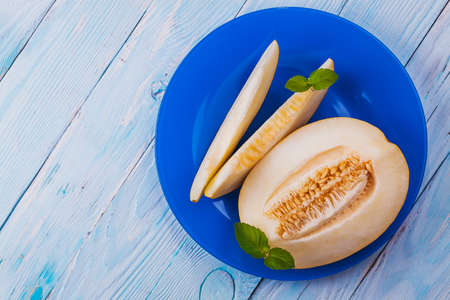 Fresh sweet orange melon in blue plate on the white wooden table. top viewの写真素材