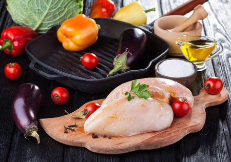 raw chicken fillets on wooden cutting board, with vegetables and pan grillの写真素材