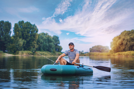 Young man fishing from the rubber boat on the pondの写真素材