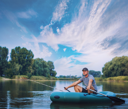 Young man fishing from the rubber boat on the pondの写真素材