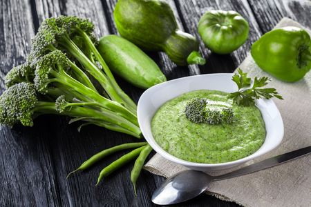 Broccoli cream soup with fresh vegetables on the black wooden tableの写真素材