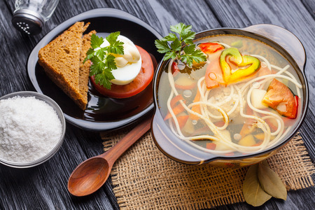 Fresh vegetable soup with noodles in a pot on the black wooden backgroundの写真素材